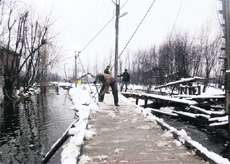 A worker of Srinagar Municipal Corporation clears a snow-covered footbridge at Merr Bhari near the Dal Lake in Srinagar on Saturday. 