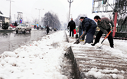 Workers of the Srinagar Municipal Corporation (SMC) clear a snow-covered footpath in Srinagar on Sunday