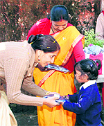Usha Bahuguna, president of the FRI Ladies Club, gives warm clothes to a student of New Forest Primary School on the FRI premises in Dehradun on Tuesday