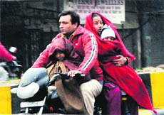 Members of a family riding a motorcycle protect themselves from cold and rain by wearing more woollens in Amritsar on Monday. 