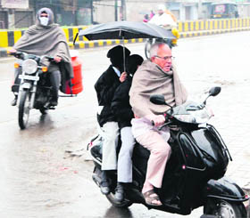  An elderly man takes children to school during rain in Amritsar on Monday.