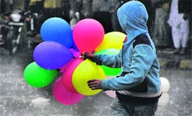 Unmindful of heavy rain, a boy plays with balloons on a road