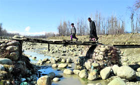 A man along with his son walks on a damaged bridge at Panzan village in Chadoora area of Budgam district on Friday.