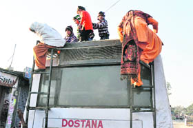 Passengers climb on to and get down from a bus rooftop near the busy Satwari Chowk in Jammu on Monday. Traffic policemen, who are hand in glove with the transporters, turn a blind eye to such gross violation of safety norms.