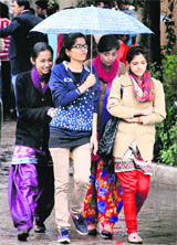 Girls huddle together under an umbrella to protect themselves from rain. 