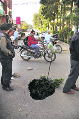 Commuters pass a hole after a portion of the Pakhowal Road in Ludhiana caved in on Saturday. 