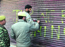Policemen remove a graffiti written on the shutter of a shop on the Residency Road in Srinagar on Friday. 