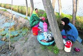 Women wash utensils near a stream in Budgam, west of Srinagar, on Tuesday.