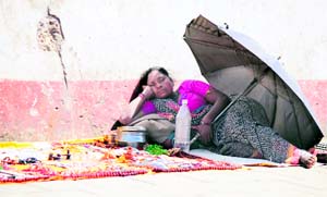 A roadside vendor takes a nap under the umbrella on a busy road in Jammu on Thursday. 