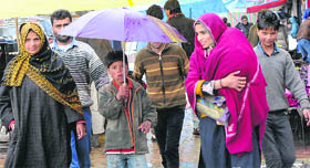 Pedestrians walk amid rain in Srinagar on Sunday.