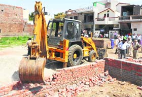 A JCB machine pulls down a boundary wall in the Joshi Nagar area at Haibowal in Ludhiana on Tuesday
