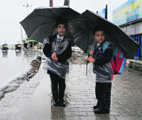 Boys with umbrellas wait for their school bus in Srinagar on Tuesday.