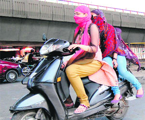 Girls cover their faces while riding a scooter on a hot summer day in Amritsar on Tuesday.