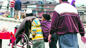 Young boys push a wheelchair carrying a man as they seek alms on a road in Srinagar.