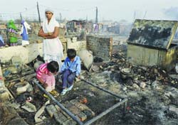 Residents of the slum at their burnt shanty which had gutted in a fire in Bawana, New Delhi, on Friday. Tribune photo