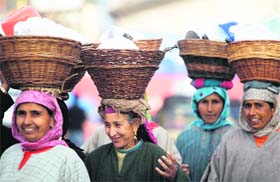 Enjoying the work: Women in Kashmiri attire carry wicker baskets on their heads, while selling goods in busy streets of Srinagar on Sunday