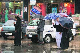 Students wait for a bus during incessant rain in Srinagar on Tuesday