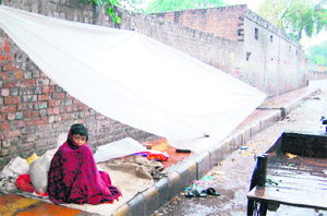 A boy protects himself from rain by sitting under a plastic sheet in Amritsar on Friday.