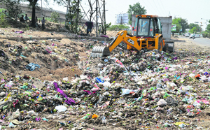 An earthmoving machine lifts garbage from a collection point near the Dugri Road intersection in Ludhiana.