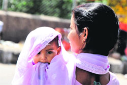 A woman covers her child with a dupatta on a sunny day.