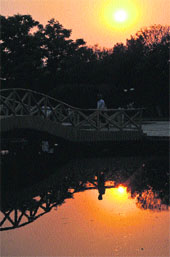 A man moving on a bridge as the setting sun is reflected in water in Atal Park in Karnal.