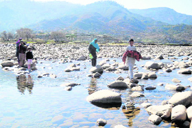 A boy carrying a baby crosses the stream at Chajjla village in Poonch on Wednesday.