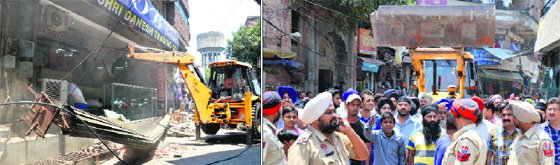 An earthmoving machine demolishes an illegal shutter in the Niggar Mandi area and shopkeepers raise slogans against the MC.