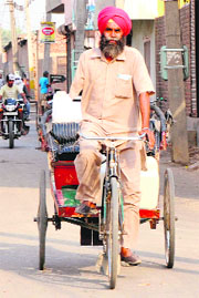 Munshi Singh (47) pulling a cycle-rickshaw with his left arm on a city road.