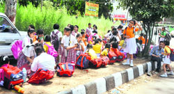 Students of a prestigious school wait for the school bus on a footpath under the sweltering sun in Jammu on Wednesday. 