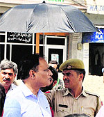 A policeman, supposed to provide security to the Jammu Divisional Commissioner, holds an umbrella for him in Jammu on Saturday