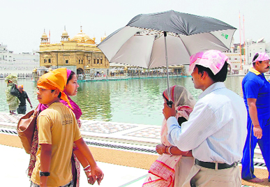Devotees walk under an umbrella to escape heat at Golden Temple in Amritsar. 