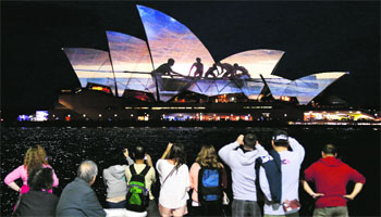Visitors look at a photograph projected onto the sails of the Sydney Opera House during a display showcasing photographs taken by members of the public depicting their daily lives.