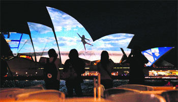 A group of women look at a photograph projected onto the sails of the Sydney Opera House.