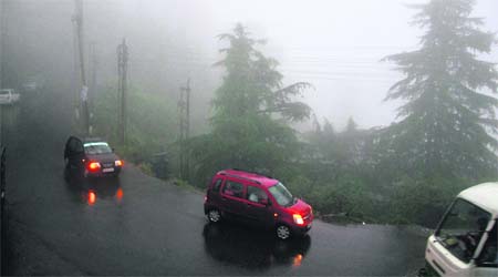 Vehicles move slowly in a dense fog during heavy rainfall in Shimla on Monday. 
