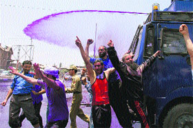 Government employees raise slogans as a police vehicle fires a jet of dyed water at them during a protest in support of their demands in Srinagar on Monday.