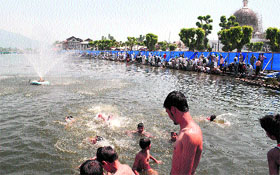 Children enjoy a swim at Dal Lake in Srinagar to get relief from the scorching sun on Monday.