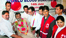 Members of the Red Cross Society felicitate Gamgeen Majeed Narbali, a teacher and social activist, for donating blood for the 100th time on World Blood Donation Day in Srinagar on Friday.