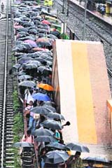 Commuters walk under umbrellas during rain at a railway platform in Kolkata on Friday