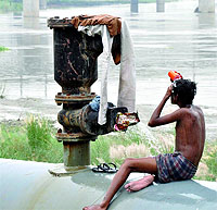 A man having a bath from a leaking waterline to escape from the heat near ISBT in New Delhi on Tuesday