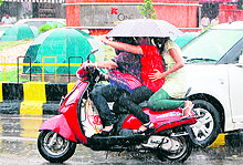 Girls riding a scooter protect themselves from rain by holding an umbrella in Amritsar on Friday