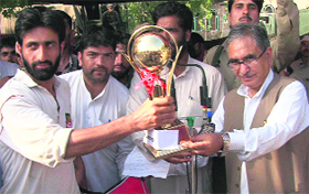 Minister for Agriculture Ghulam Hassan Mir presents a trophy to the winners of a local cricket tournament at Pattan on Friday.