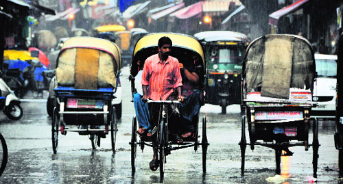 A rickshaw-puller ferries passengers during rain in Ludhiana on Tuesday.