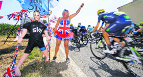 A spectator dressed in the colours of the Union Jack reacts next to an inflatable doll with the mask of Team Sky rider Christopher Froome of Britain as the pack of riders cycles on its way.