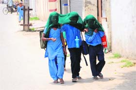 Schoolchildren cover their faces to escape the heat while returning home