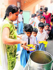 A teacher serves food to students of Mandi Fanton Ganj Government School on Friday. 