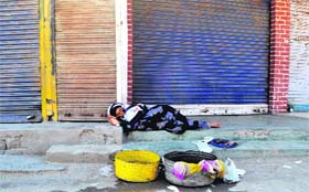 Waiting for customers: A woman, who sells fish, sleeps in front of closed shops after the curfew was lifted in Anantnag on Sunday