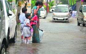 A woman, along with her children, wades through a flooded street near the Rani Jhansi road