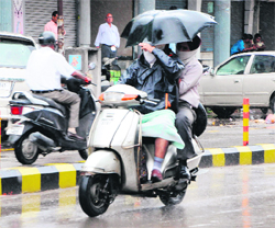 Youngsters carry an umbrella while riding a scooter to protect themselves from rain in Amritsar on Sunday.