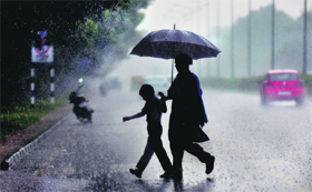 A woman helps her son cross a road on a rainy Monday afternoon in Chandigarh.