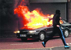 A protester runs past a burning car during rioting in the centre of Belfast, Northern Ireland, on Friday